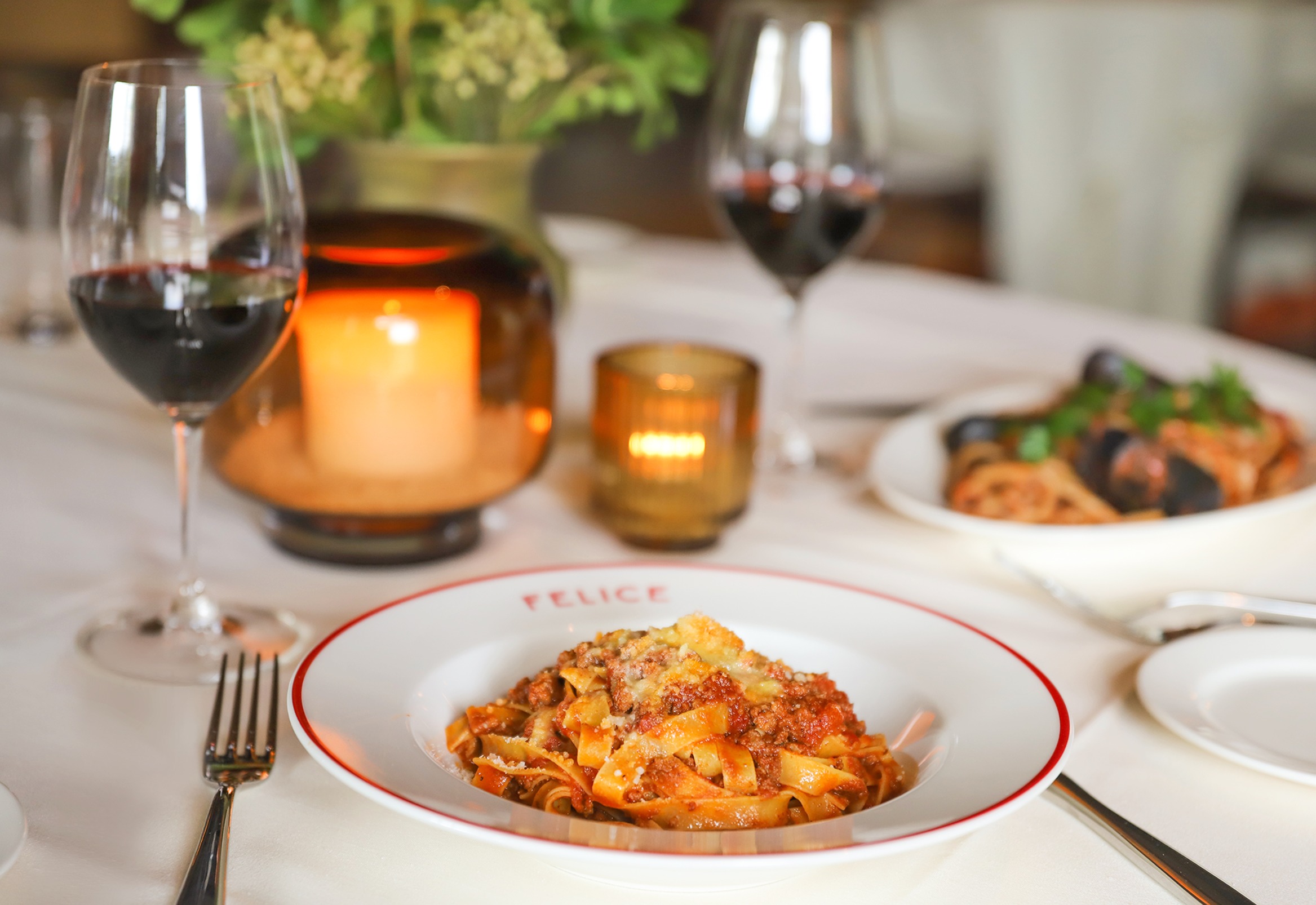 Fresh ribbon pasta with a hearty meat ragu topped with grated Parmesan, served on a Felice branded plate with candlelight and wine.