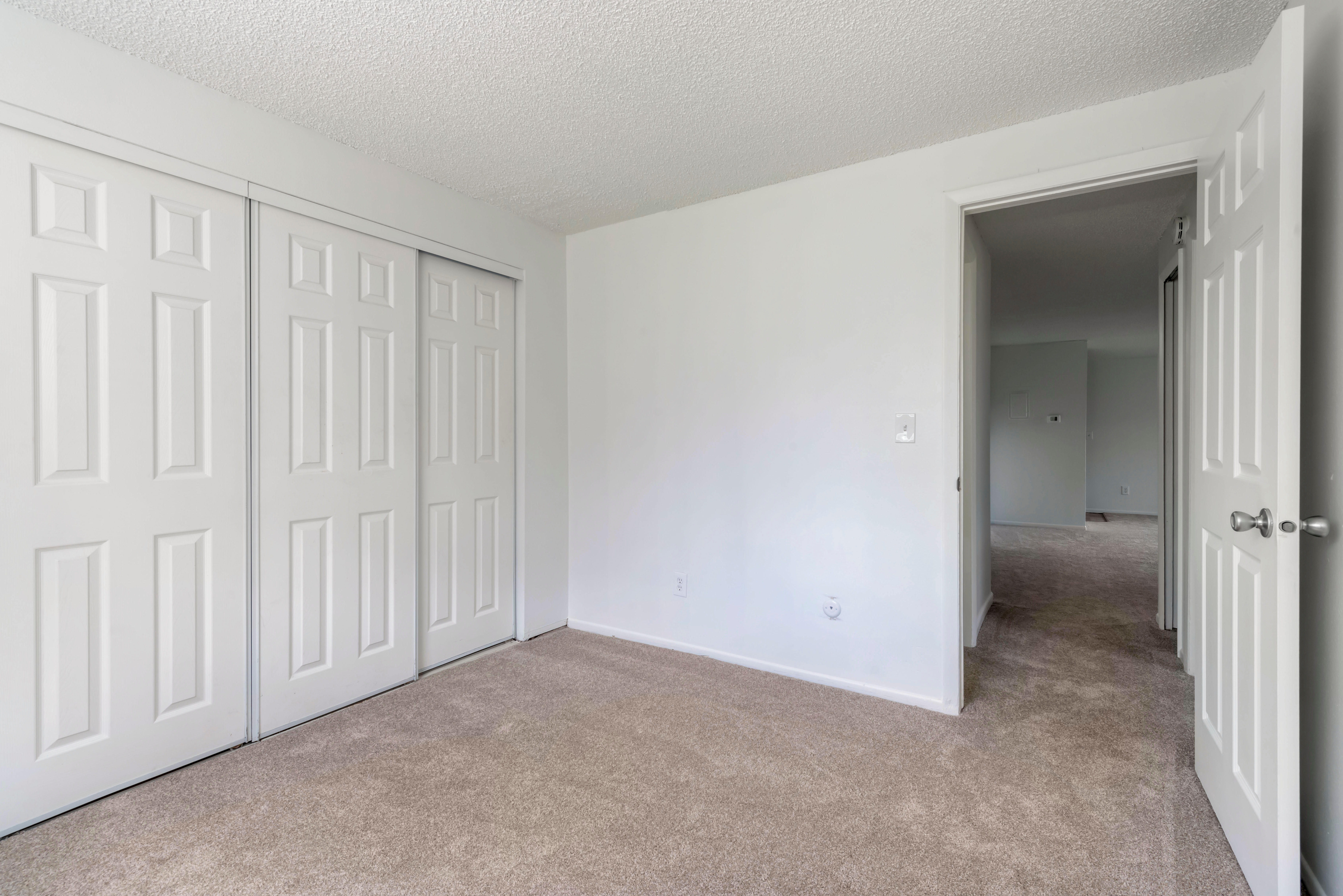 Carpeted bedroom with three sliding door closet and view to living area.