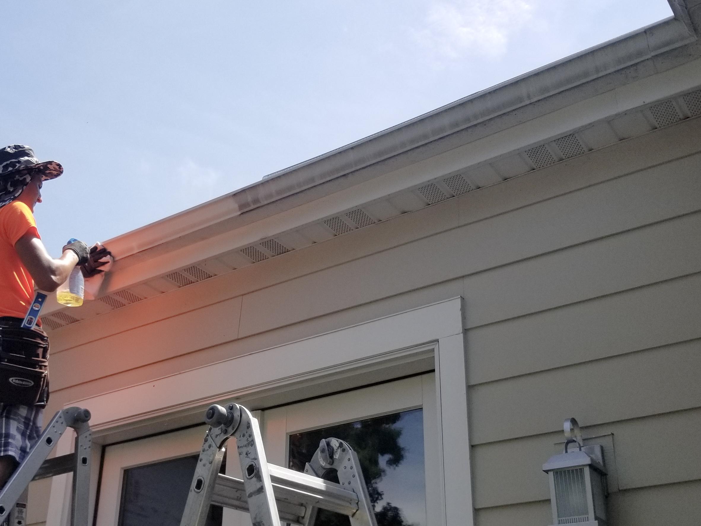 An Ultimate Gutter Solutions professional on a ladder cleaning the exterior of a white gutter.