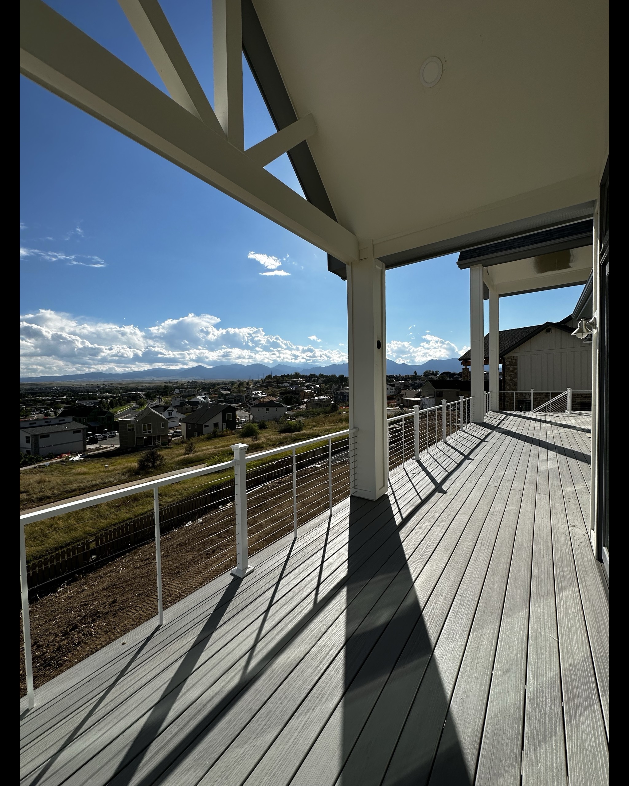 A deck overlooking the mountains with two roof covers over the deck. The deck has White ALX Cable railing with PVC Decking.