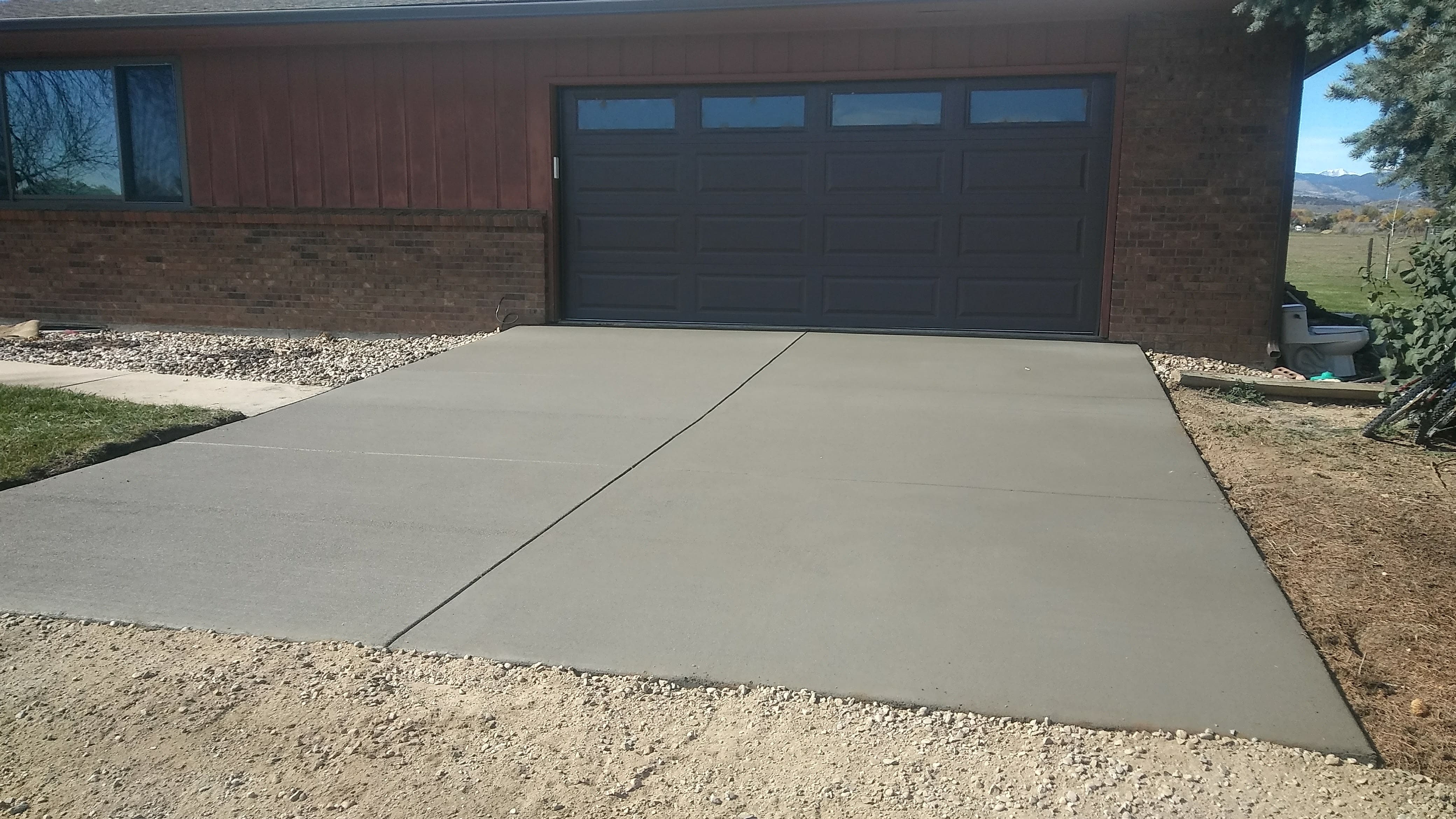 Residential concrete driveway installed in front of a two-car garage, featuring a clean broom-finished surface and properly spaced control joints.