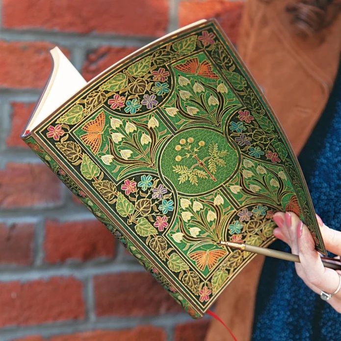 An exquisite product image by Tabula Rasa Social Stationers showcasing a Paperblanks "Poetry in Bloom" journal. The journal's cover features a captivating, intricately designed cover with lush green and gold botanical patterns intertwined with colorful butterfly motifs, embodying Paperblanks' signature blend of artistry and craftsmanship. A hand is shown holding the journal open with a pen, emphasizing its high-quality, acid-free paper, perfect for writing, sketching, and capturing thoughts. This journal transforms everyday note-taking into a celebration of creativity and heritage.