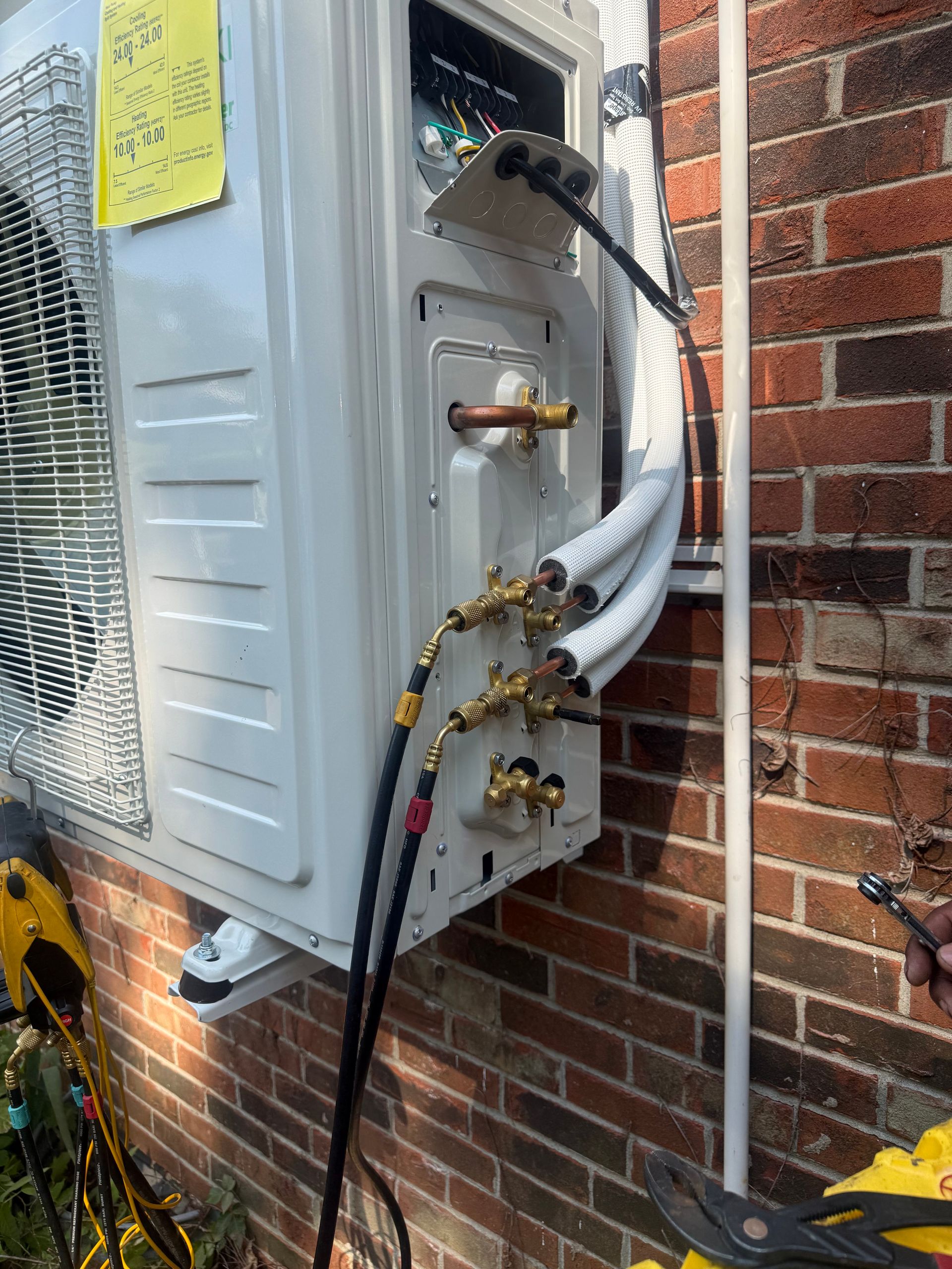 Close view of an outdoor HVAC unit during service, showing refrigerant hoses connected to brass serv 