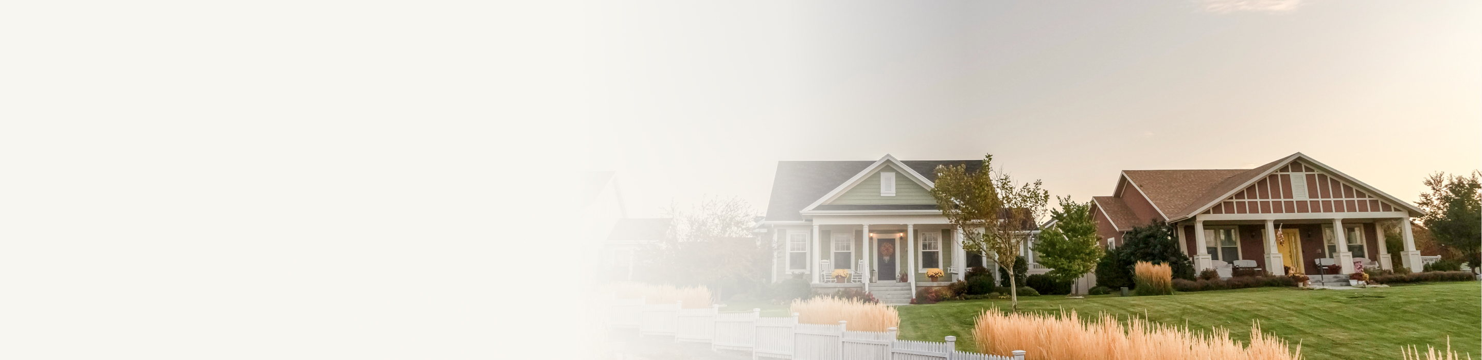 Two well-maintained detached family homes and their shared front lawn surrounded by a white picket fence.
