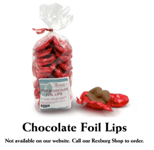 This photograph showcases Florence's Exquisite Chocolates' "Premium Chocolate Foil Lips," likely from their Rexburg, Idaho location. The main focus is a clear bag filled with red foil-wrapped chocolate lips, tied with a festive red bow. The label on the bag clearly identifies the product and includes a barcode. Several loose chocolate lips, still in their red foil wrappers, are scattered next to the bag, with one unwrapped to show the milk chocolate detail.