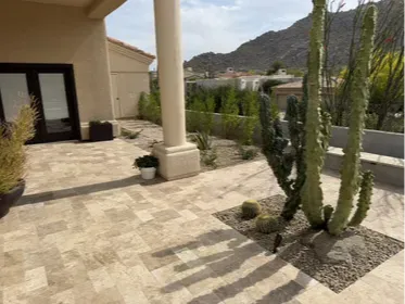 Scottsdale travertine patio with desert landscaping, Camelback Mountain in the background. Low-water xeriscape design with saguaro, ocotillo, and desert accent plants set in decomposed granite. The travertine runs continuous from the covered porch to the open patio, no breaks, no transitions. Built by Hacienda Outdoors, ROC #325952.