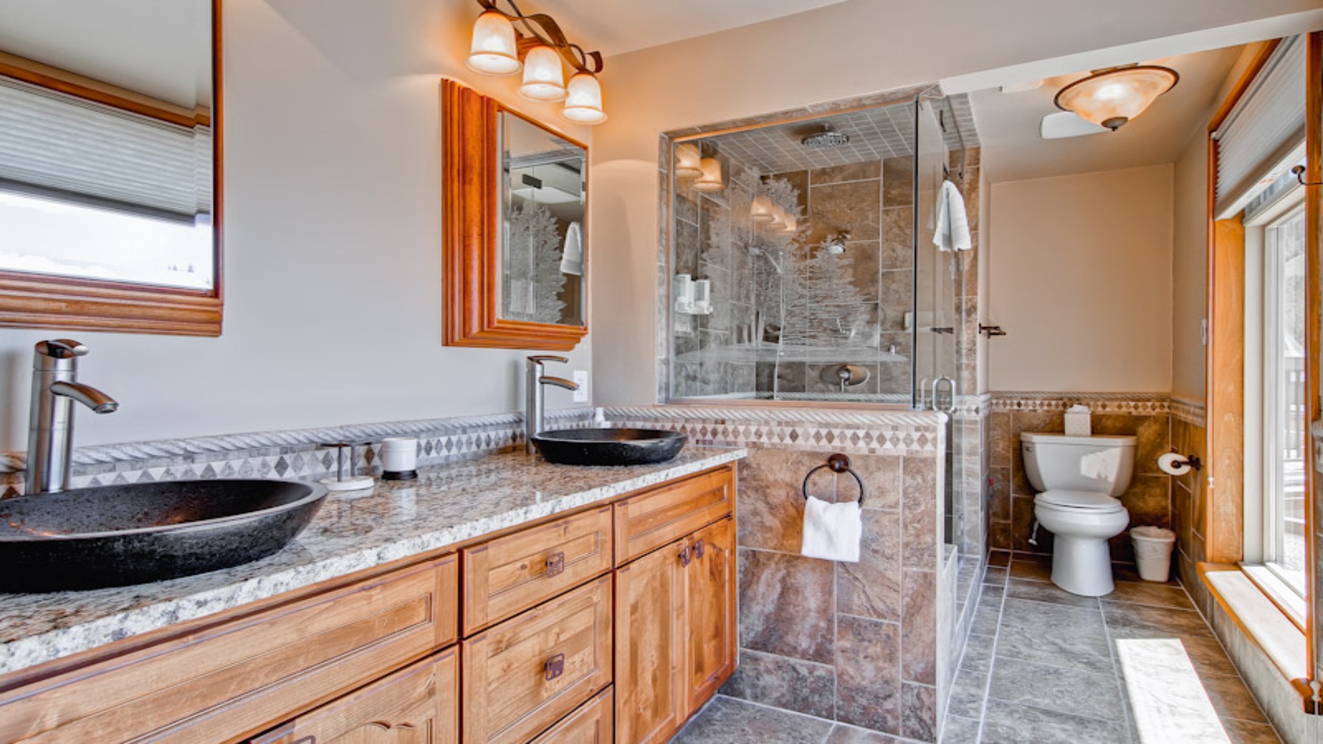 A luxurious bathroom with granite countertops, twin vanities, walk-in shower, and toilet at Vail Spa 
