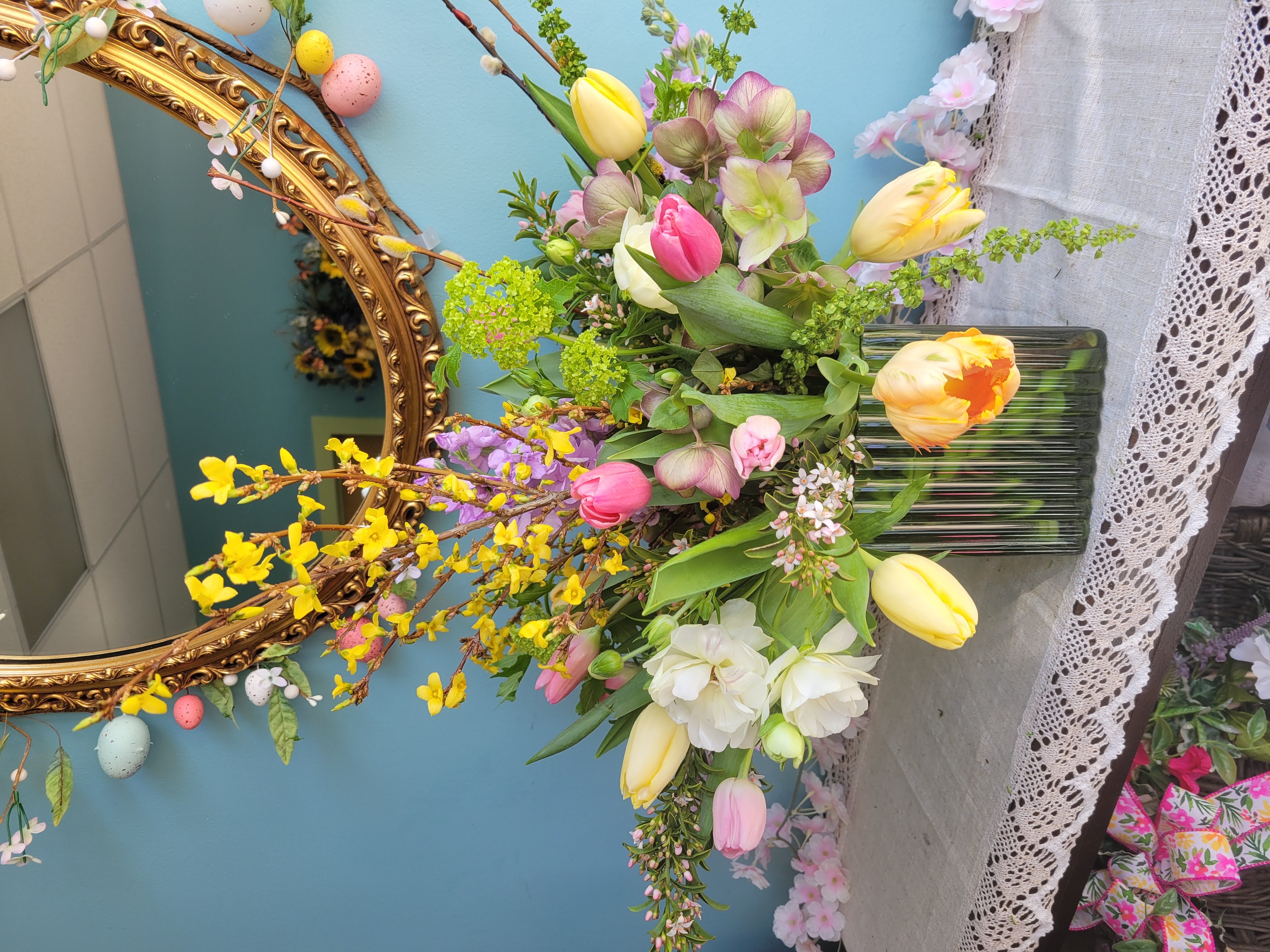 Spring table centerpiece in glass square vase with tulips, parrot tulips, hellebore, butterfly ranunculus, viburnum, and forsythia