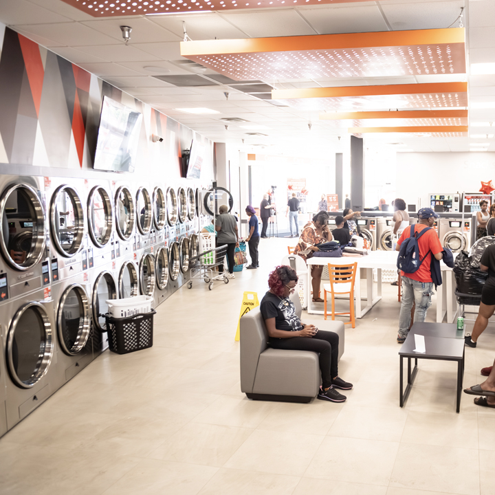 Spacious Speed Queen Laundry interior with customers using washers, dryers and seating areas. 