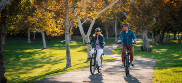 A man and a woman riding on their Pedego electric bikes through a park