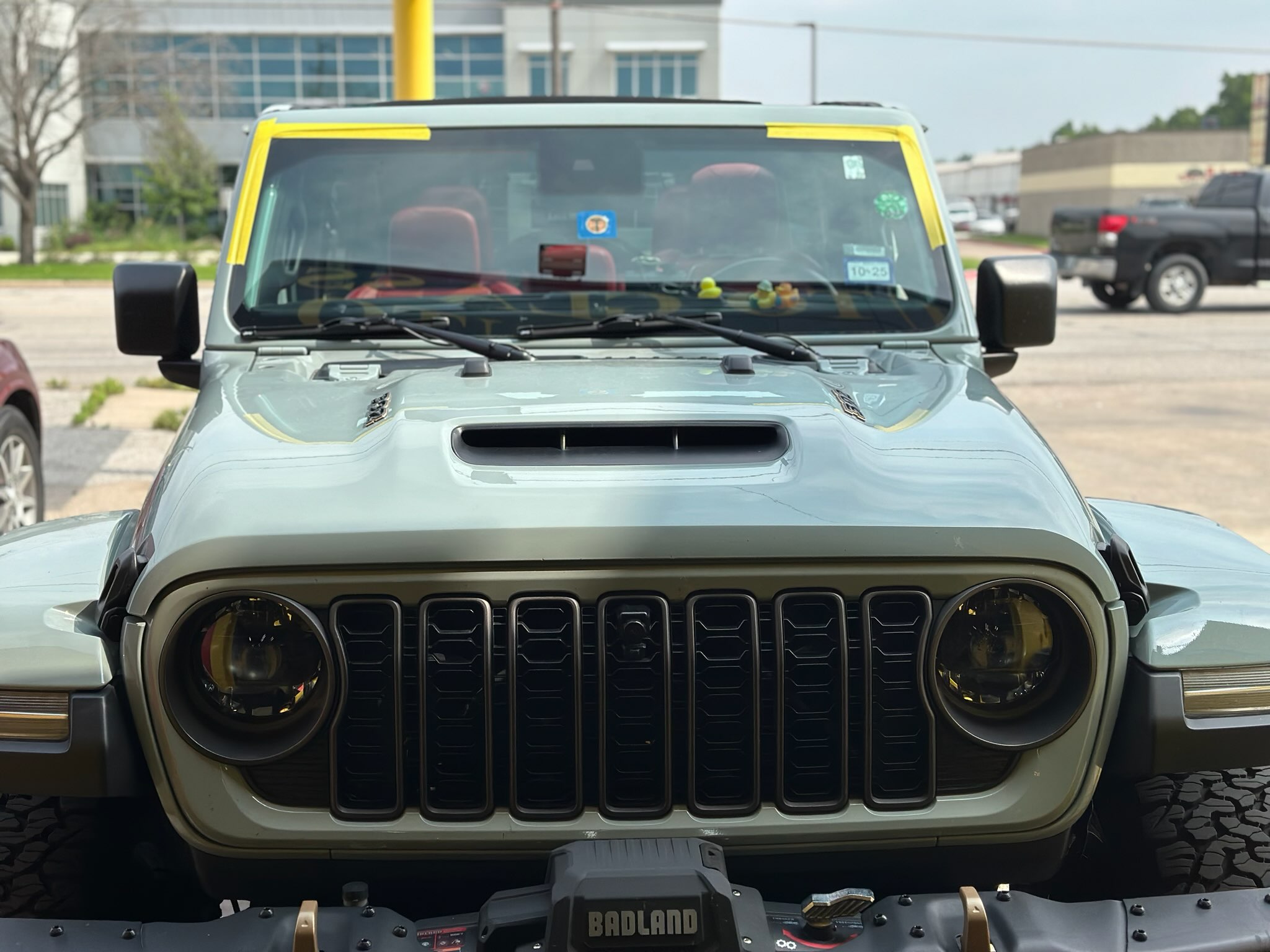 Front view of a Jeep with protective tape positioned along the upper windshield edges following installation. The image shows a windshield replacement during the final stages of the service process.