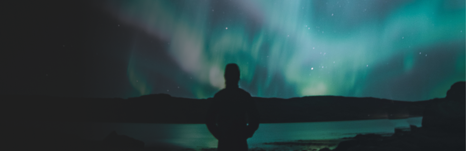 Silhouette of a person standing in a mountain landscape at night and admiring the aurora borealis.