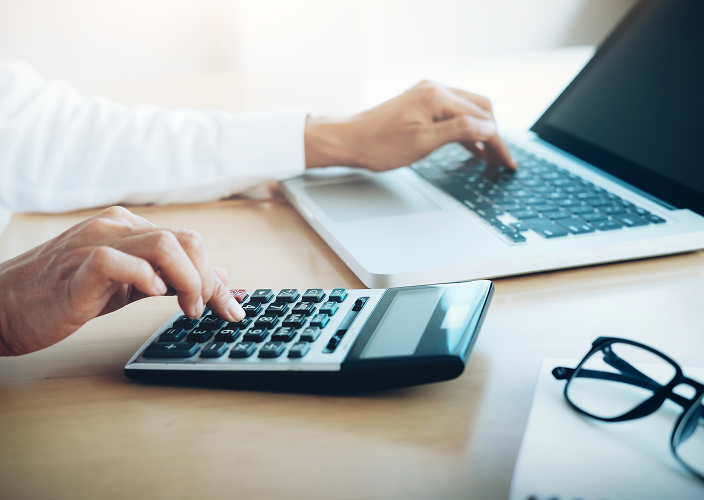 An individual typing on a laptop and calculator.