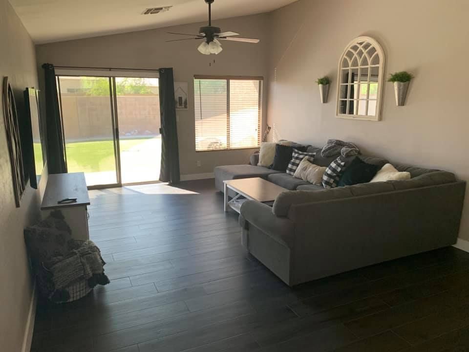 A spacious living room features dark hardwood floors, a large gray sectional couch with patterned pi 