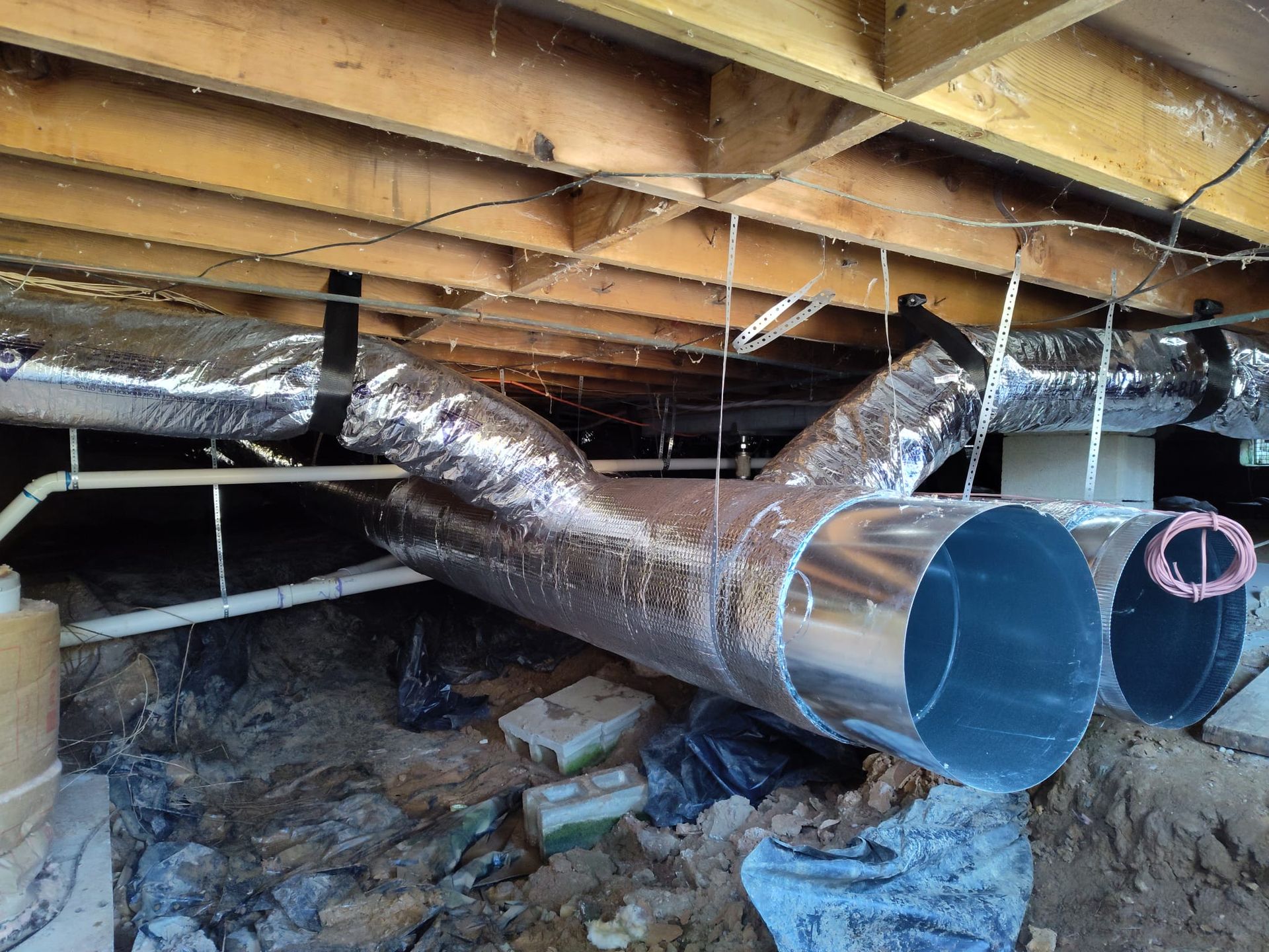 Crawlspace HVAC duct installation showing insulated trunk lines and flexible branch ducts suspended  