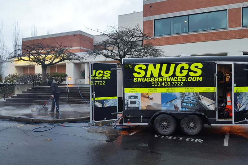 Snugs Services technician performing professional exterior building cleaning at a commercial propert 