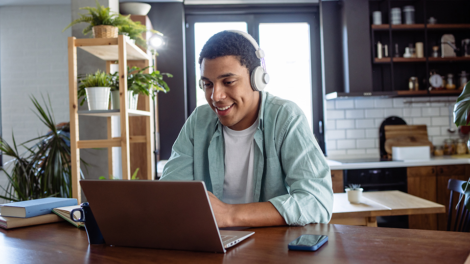 A man wearing headphones sitting at a table using a laptop