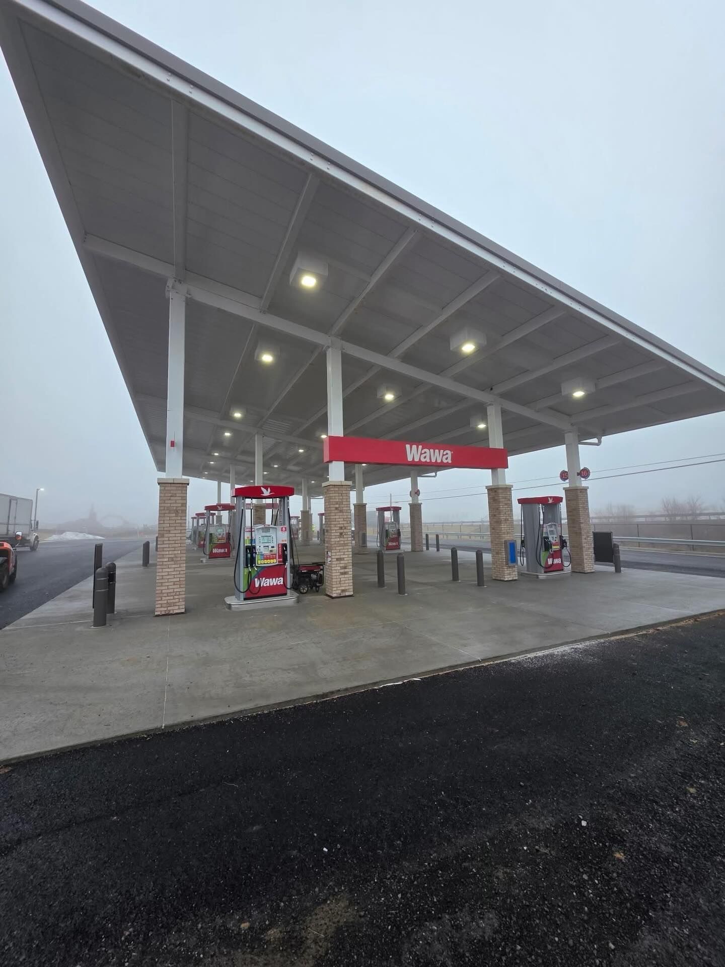 Gas station canopy with fuel pumps underneath, branded signage, and lighting, captured in foggy outdoor setting, showing clean layout of fueling area with multiple pump stations and wide coverage.