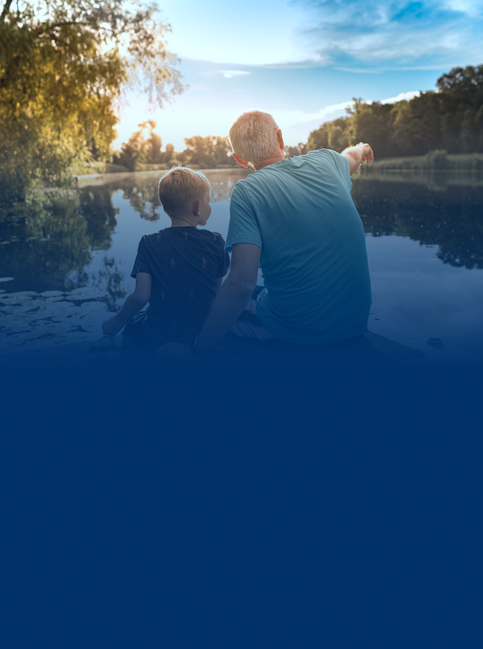 A grandfather and grandson sitting by the lake.