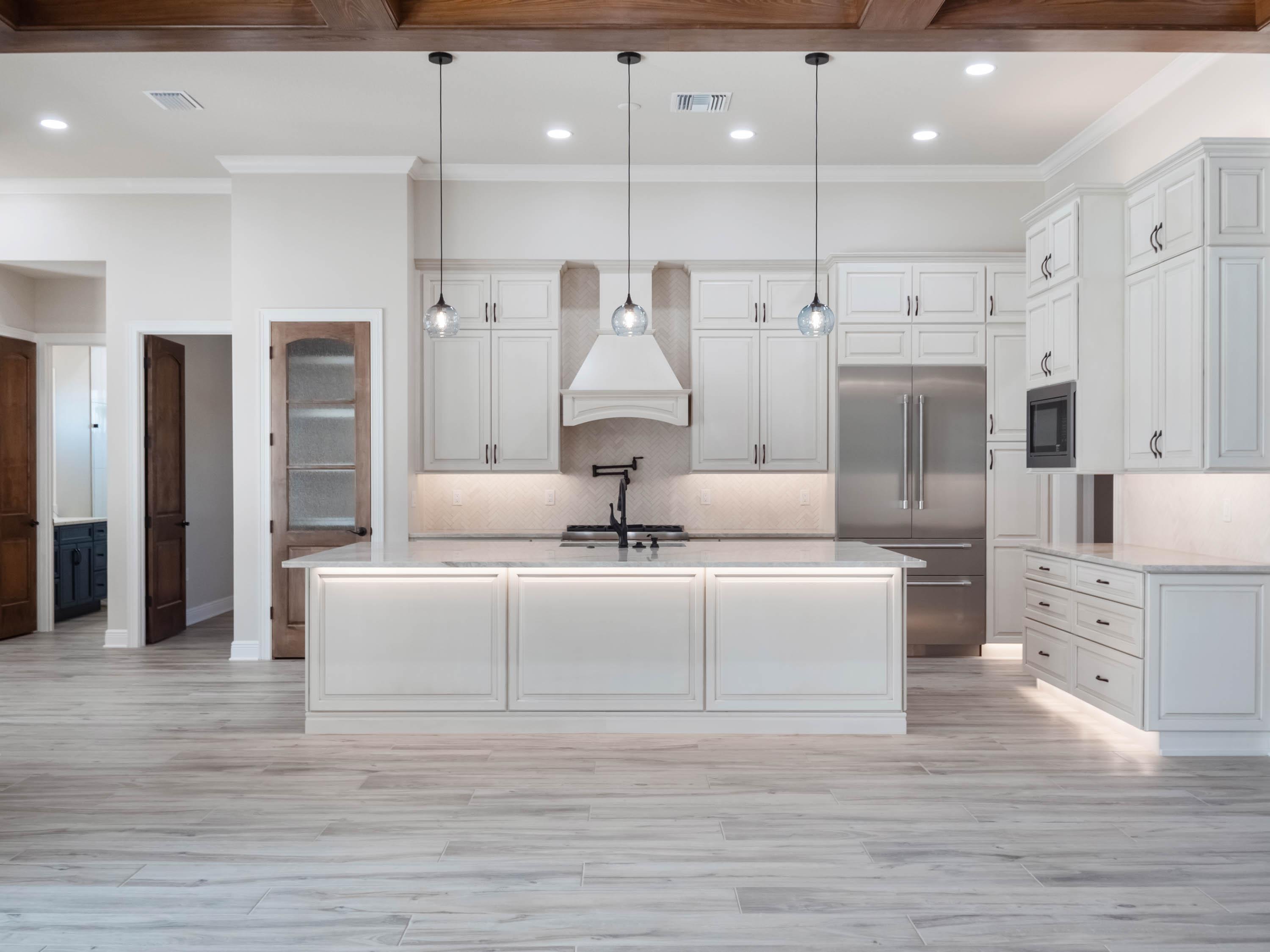 Luxury custom kitchen and open-concept living space featuring white custom cabinetry, quartz waterfall island, exposed wood beams, and premium finishes by custom home builders in Central Florida.