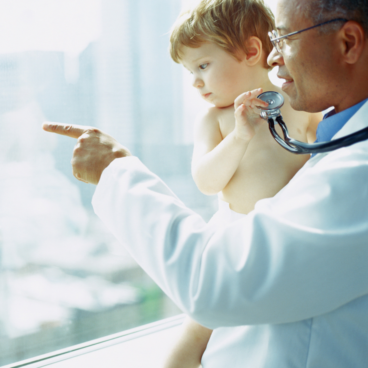 A doctor holds a stethoscope and points outside a window, holding a curious toddler. The image conveys care and curiosity in a bright setting.