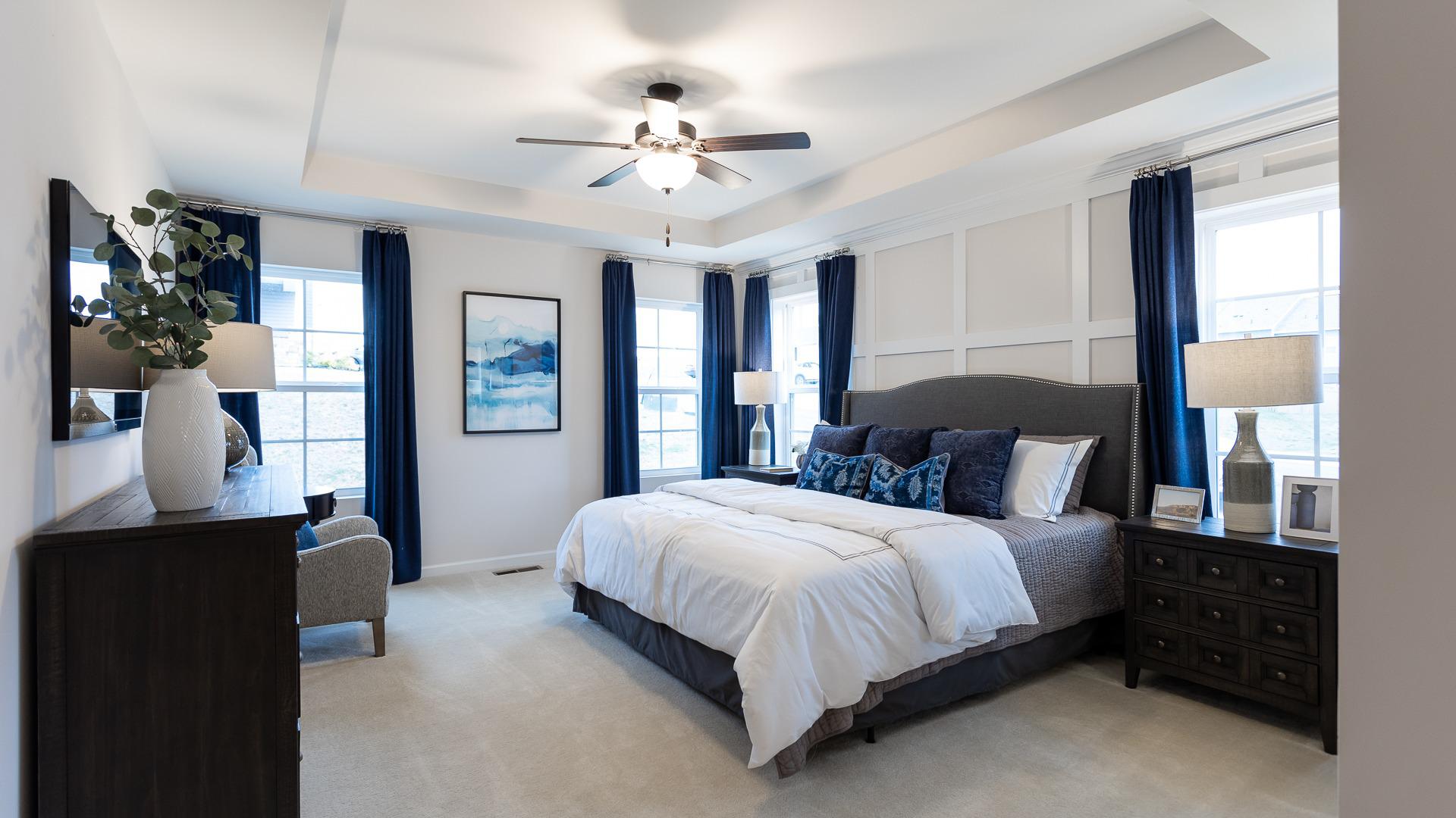 Owners' suite with king side bed, tray ceiling, four windows and ceiling fan in DRB Homes The Village of College Park