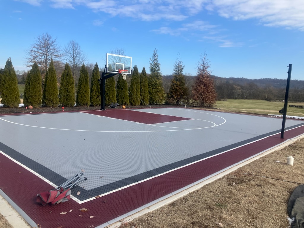 Outdoor backyard basketball court with maroon and grey tile.