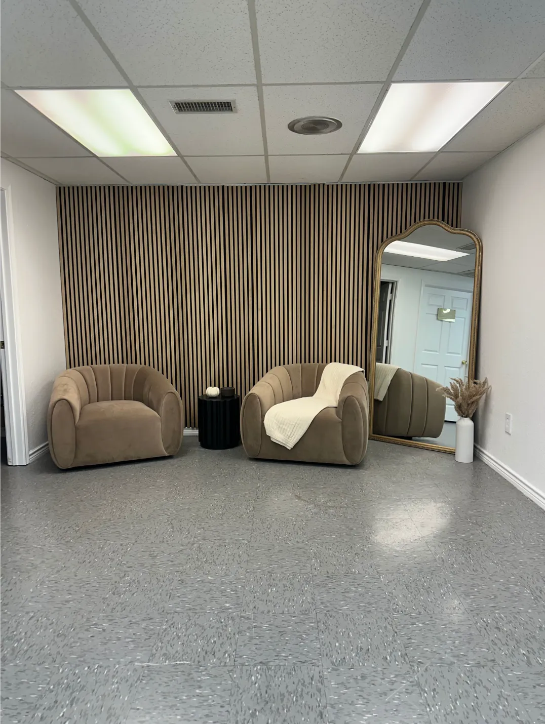 Completed office waiting area features decorative wood slat accent wall, modern lounge chairs, overs 