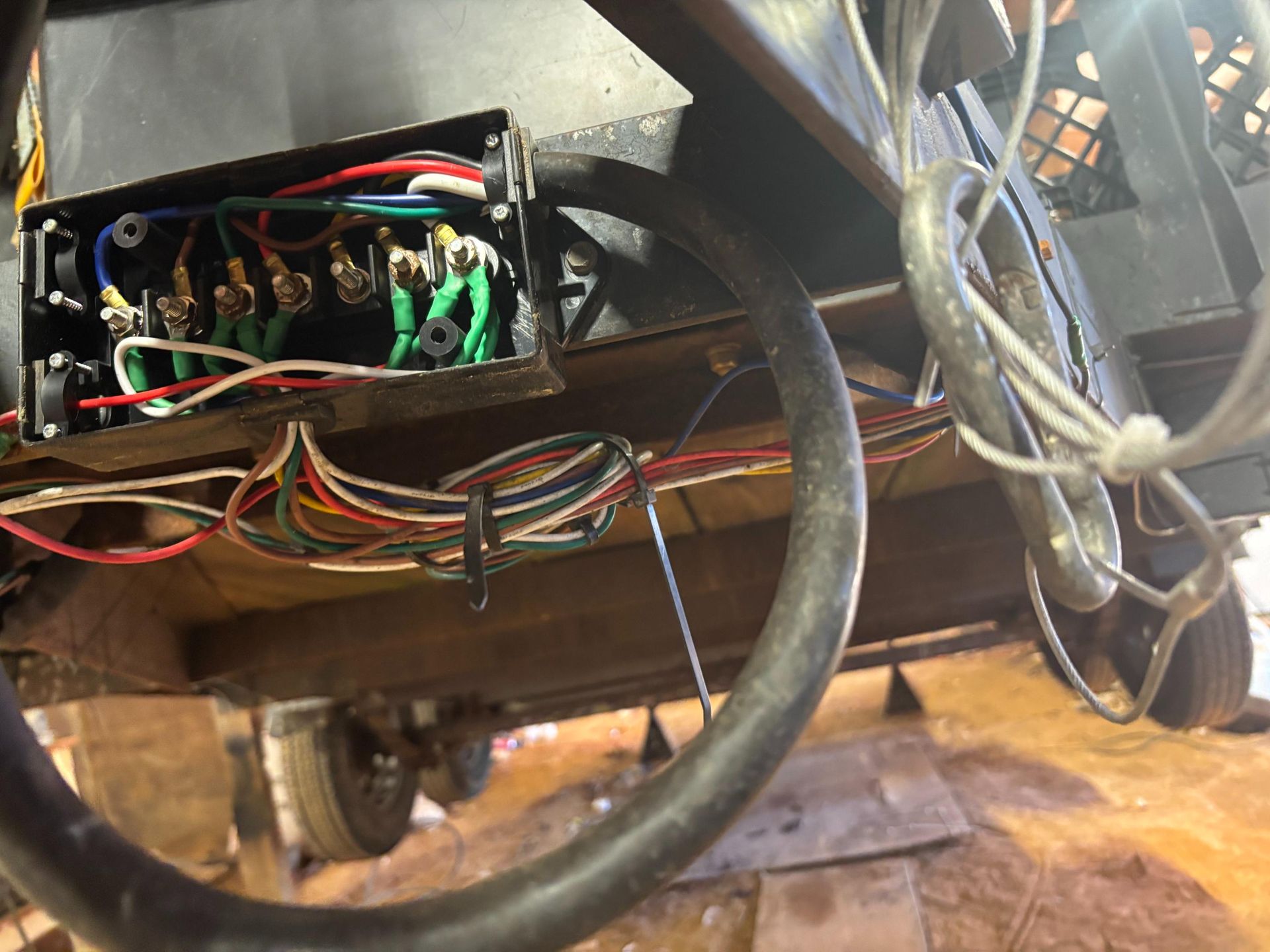 Close-up view of a trailer&rsquo;s electrical wiring junction box showing multiple colored wires connected to terminals. The setup appears installed underneath the trailer frame, highlighting wiring organization, connections, and components used for lighting or braking systems.