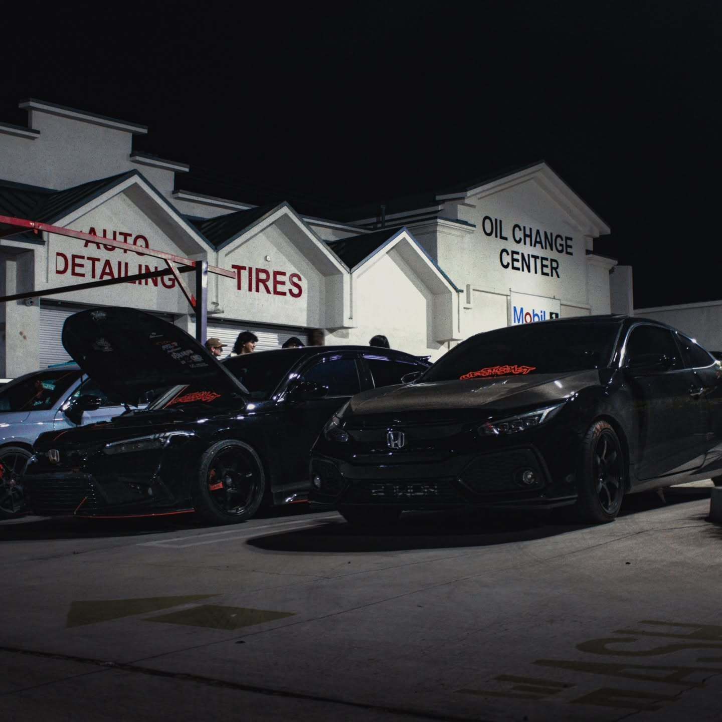Customized Honda Civic models parked at a nighttime automotive event outside an oil change center. D 