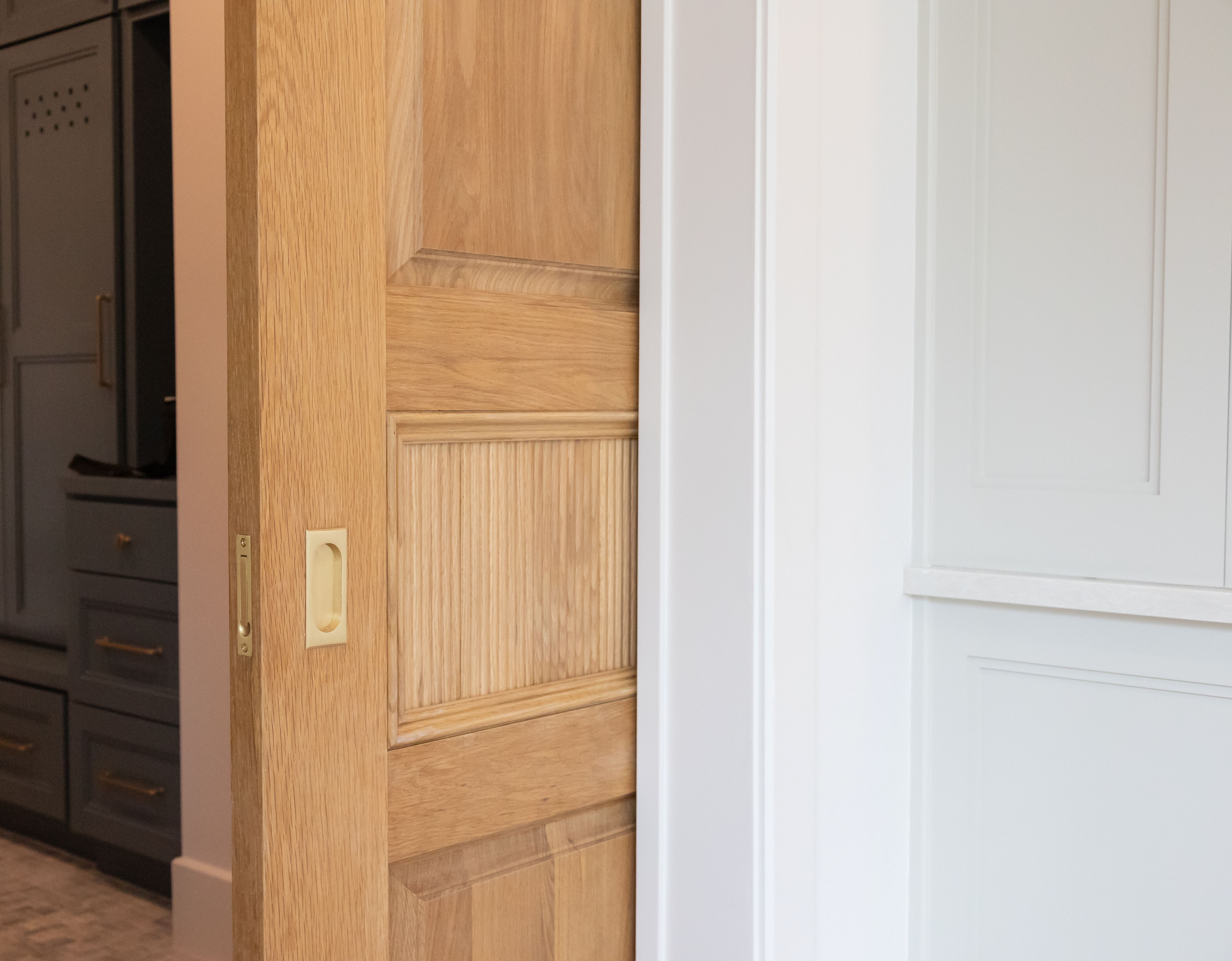 A partially open white oak pocket door showcasing the craftsmanship of the wood, leading into a stylish interior space.