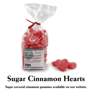 This photograph showcases a bag of Florence's Exquisite Chocolates' "Valentine Sugar Cinnamon Hearts," likely from their Rexburg, Idaho location. The clear bag allows the red, heart-shaped candies to be clearly seen, tied with a bright red ribbon. The product label identifies them as "Valentine Sugar Cinnamon Hearts" and includes a barcode. Several loose cinnamon hearts are scattered beside the bag, revealing their texture and sugar coating.