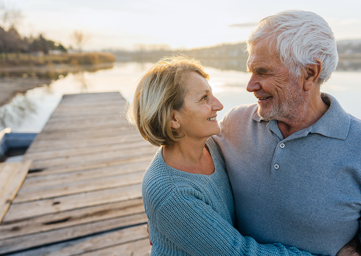 A happy elderly couple gazing into each other's eyes during sunset on a lakeside dock.