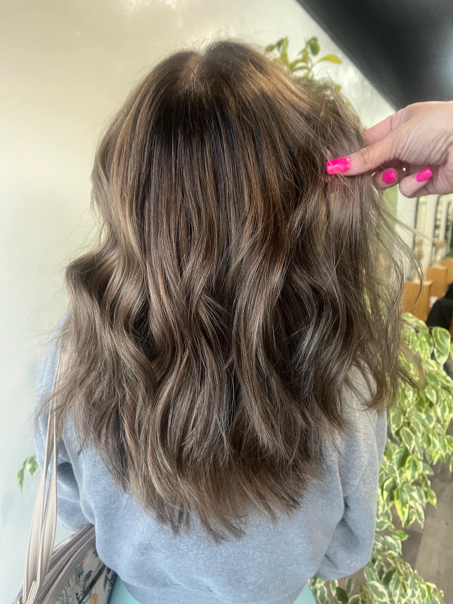 Back view of woman with medium-length brown hair featuring subtle highlights, styled in loose waves for a natural salon-finished look.