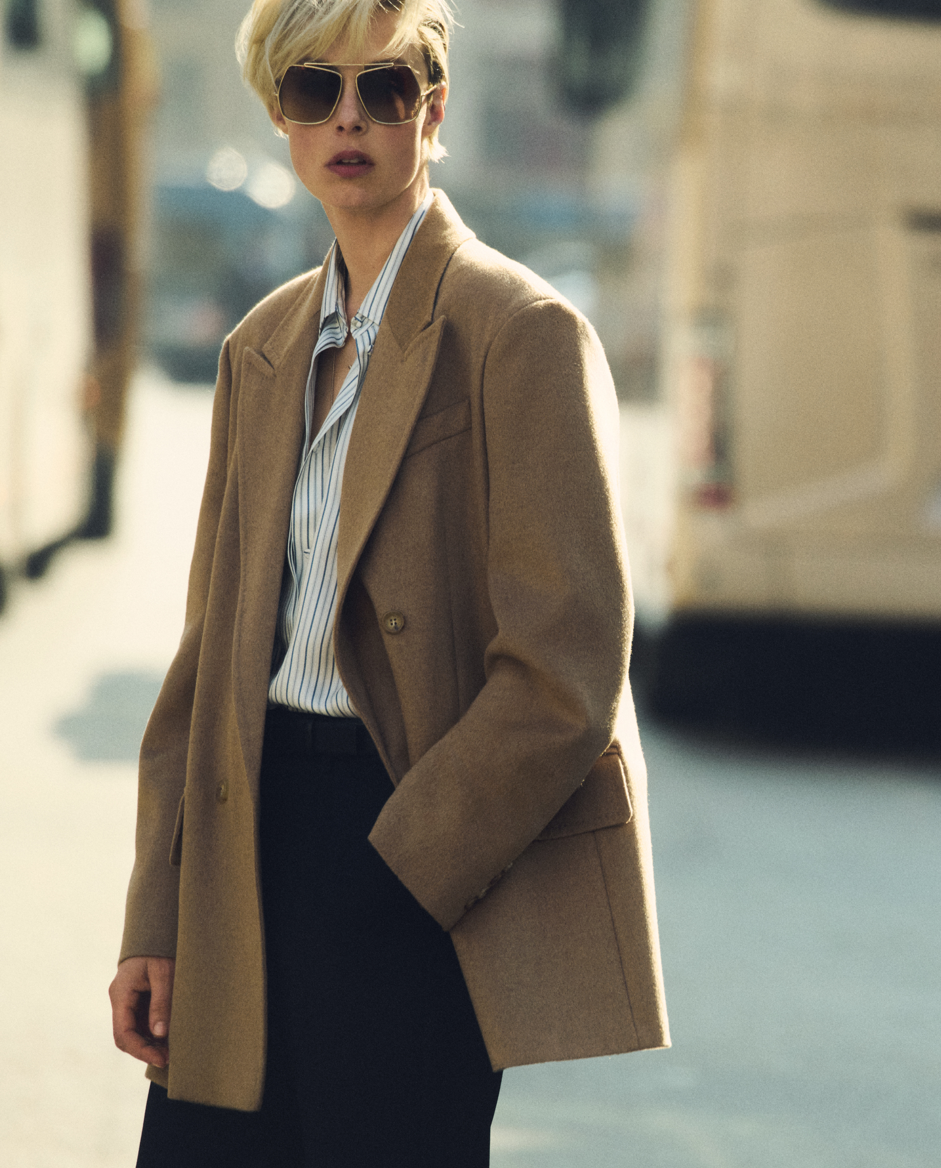 Model in double-breasted blazer-style Max Mara Olimpia Jacket in camel colour, with dark glasses and shirt in an urban environment.