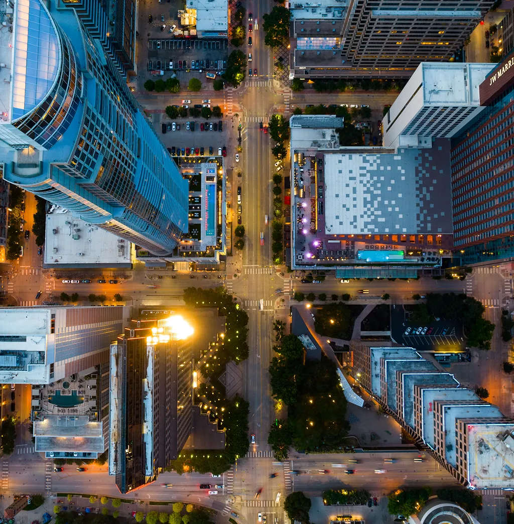 Aerial view of a city intersection with crosswalks, traffic and glass high-rise towers in golden sunlight.