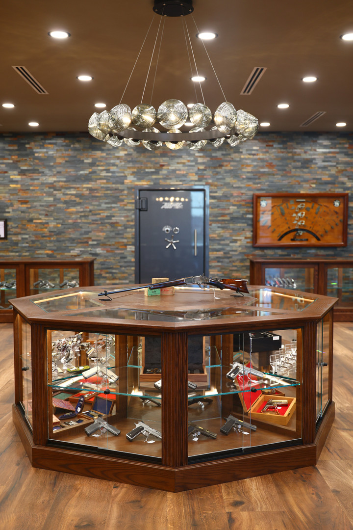 The main floor of Shoot It LLC's Phoenix showroom — a luxury retail environment featuring an octagonal display island, custom cabinetry, stone accents, and a curated collection of antique and collectible firearms.