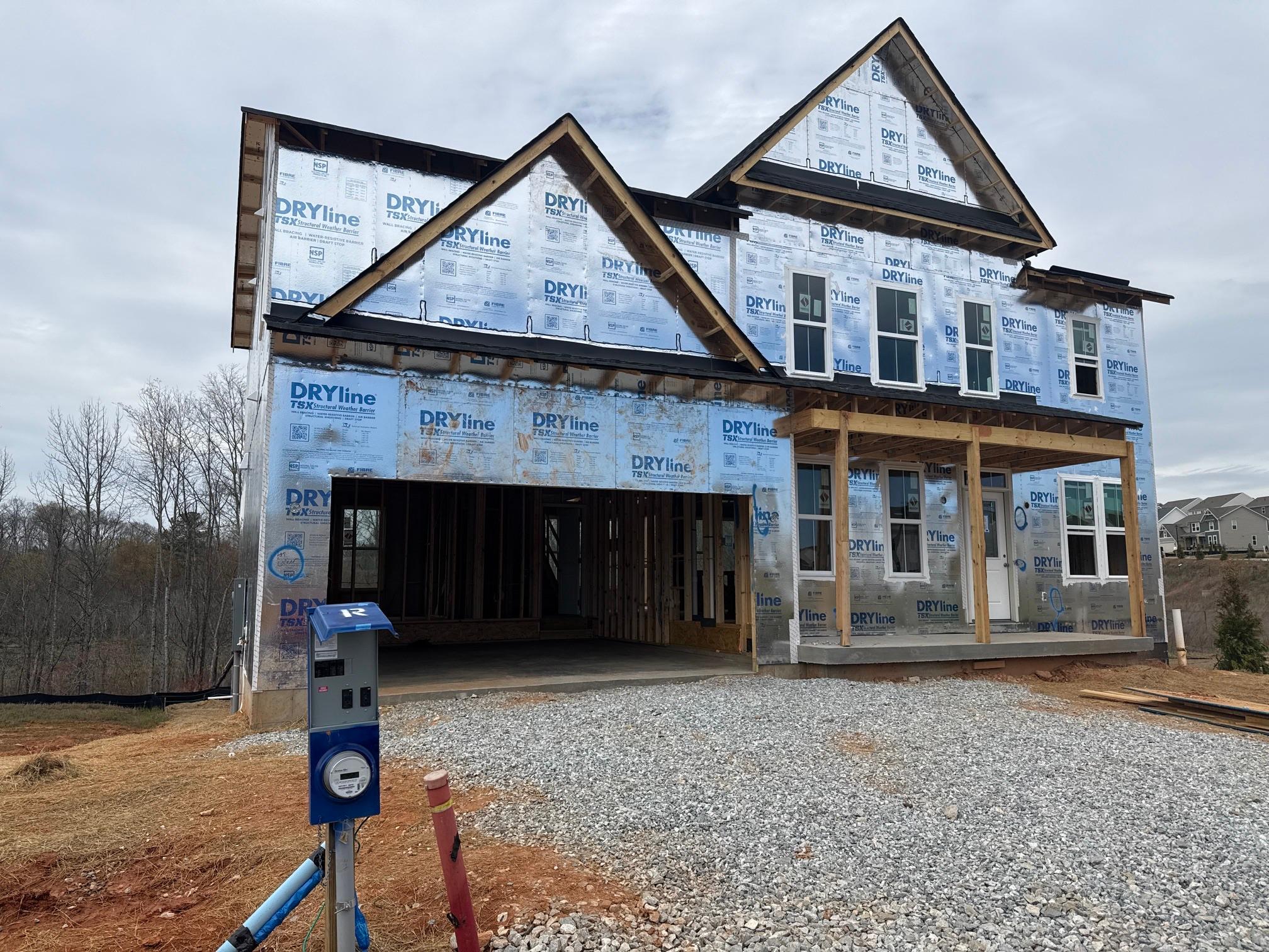 Front exterior of a new home under construction wrapped in DRYline TSX weather barrier with exposed framing, windows, and a temporary electrical meter.