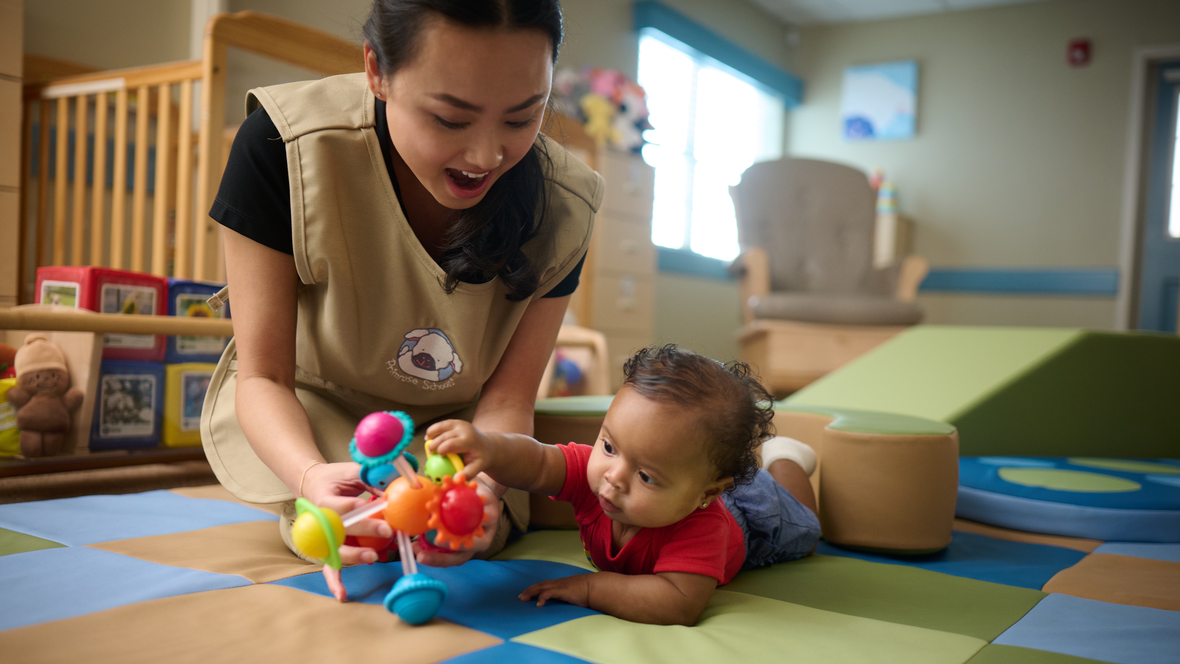 Primrose Schools infant teacher engaging baby with colorful toy during tummy time in early learning classroom