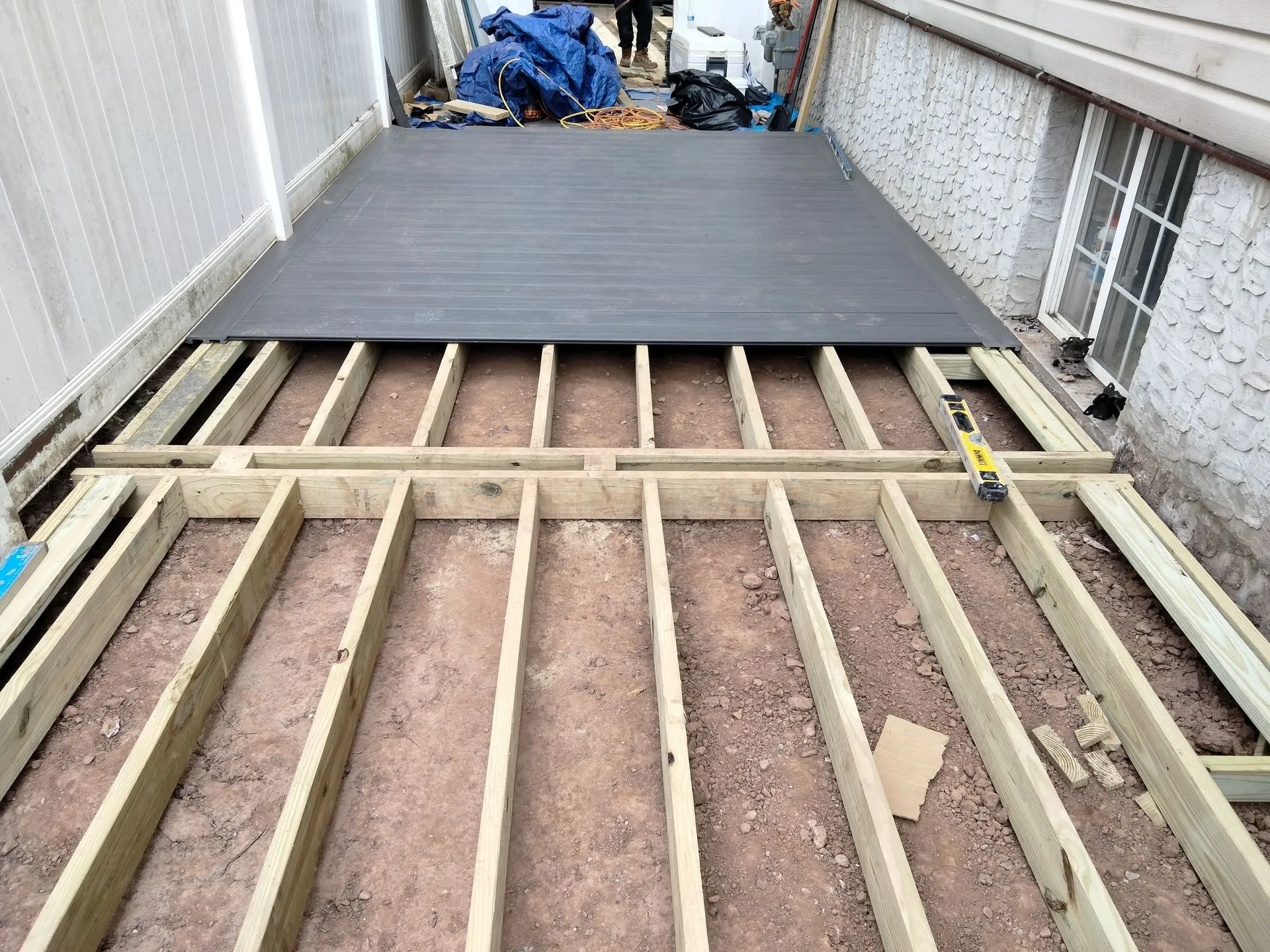 Deck construction in progress showing pressure-treated lumber joists installed between residential buildings. Composite decking boards are partially completed, highlighting structural framing, craftsmanship, and preparation for outdoor living space.