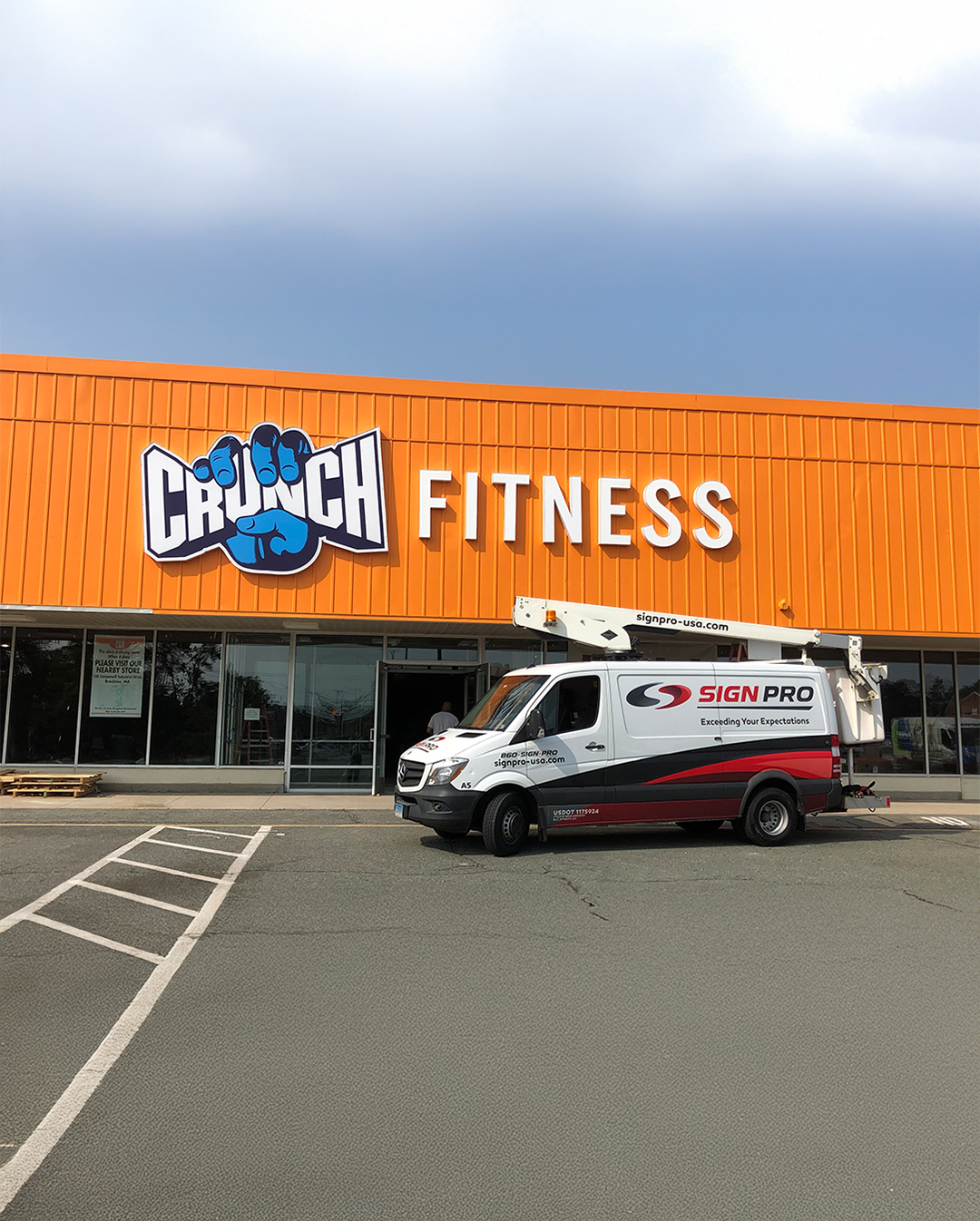 Sign Pro, Inc. vehicle and boom lift parked outside Crunch Fitness as part of a commercial signage installation, demonstrating professional branding and on-site service delivery.
