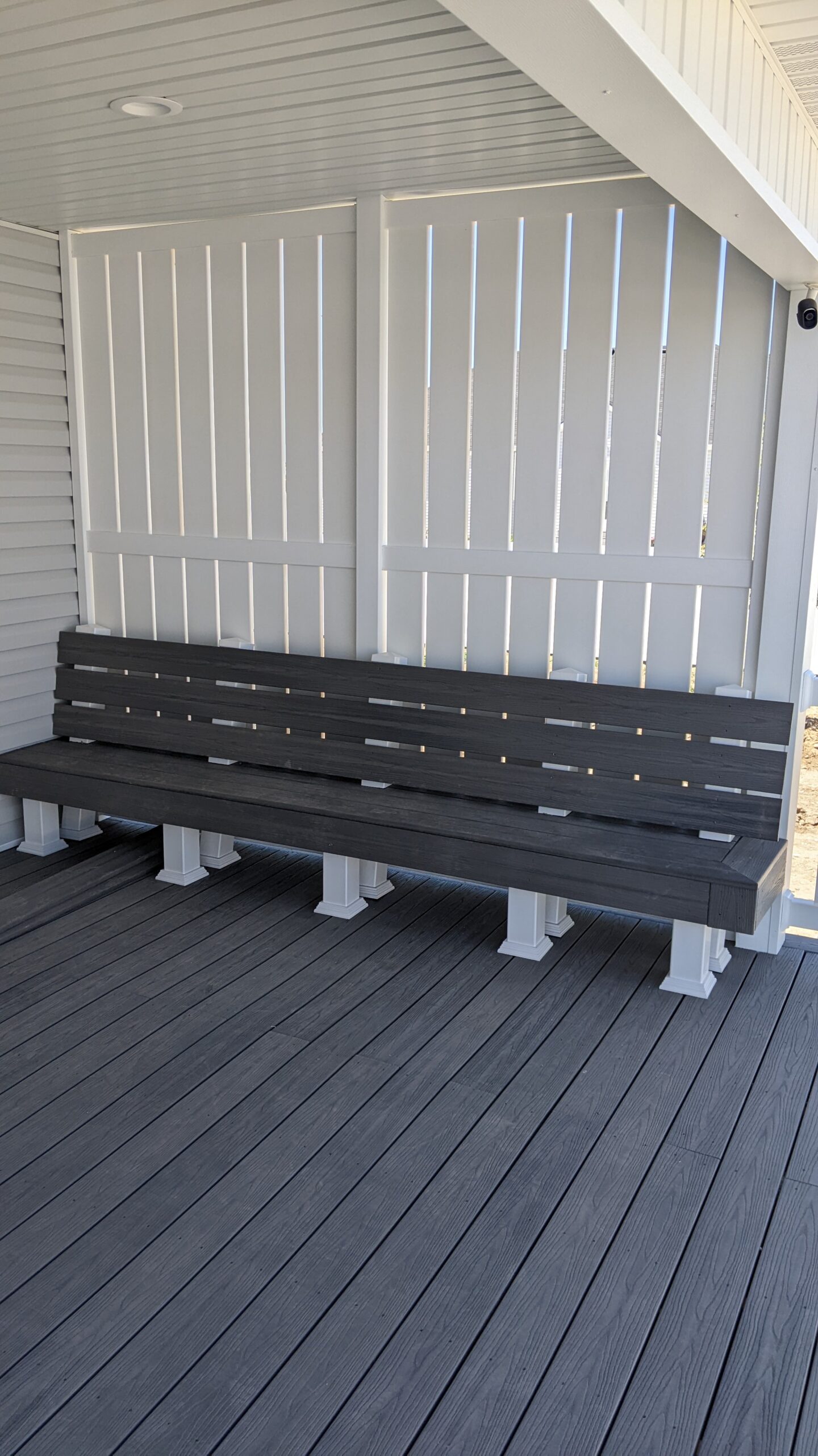 Expand your outdoor living possibilities with this custom deck by DeckPro LLC, which combines functional seating with elegant privacy. We installed low-maintenance composite decking in a modern grey tone and paired it with a unique built-in bench featuring matching grey slats and contrasting white support posts. For the ultimate in functional design, we included a stylish white vertical louvered privacy wall, creating a cozy and inviting retreat.
