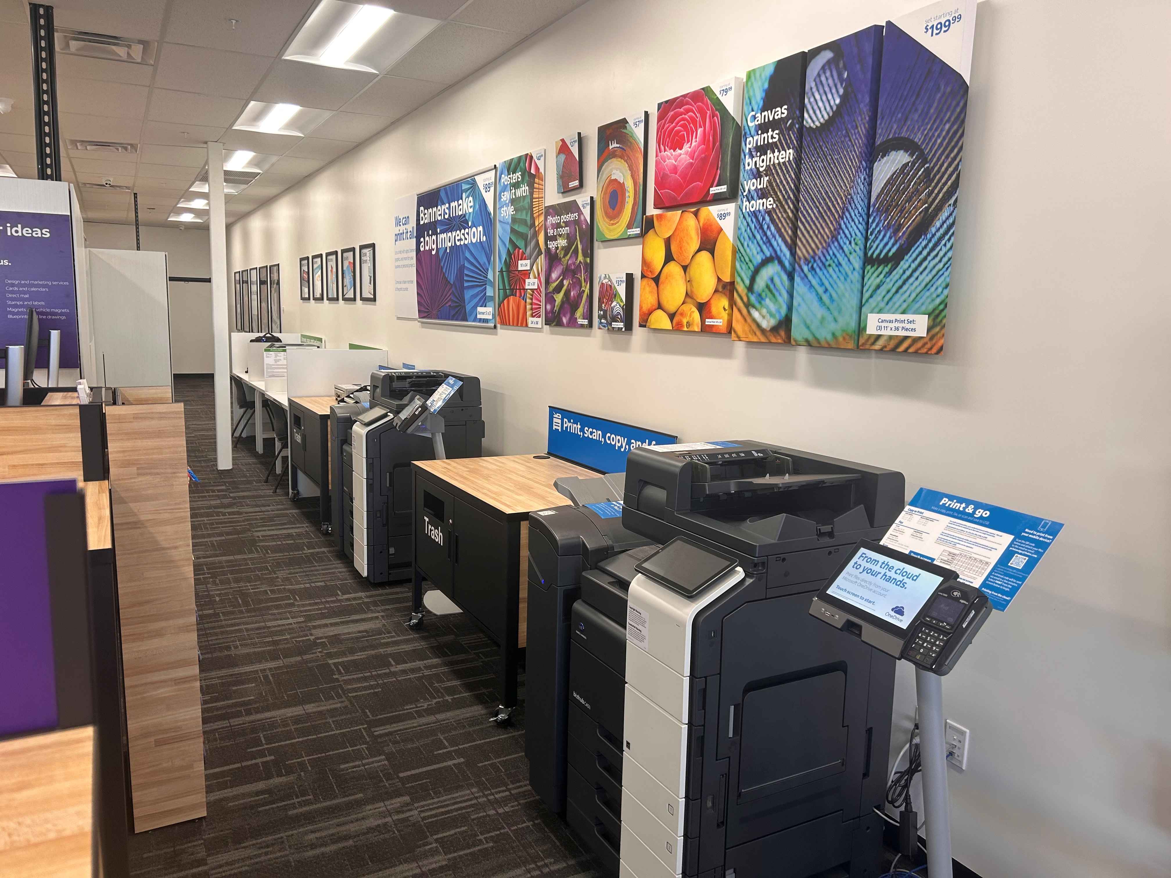 The self-service printing area with a line of professional printers and a large wall display of cust 