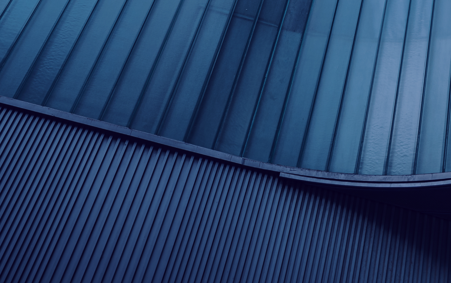 Close-up, abstract image of the exterior of a curved building with multiple levels featuring different vertical lines of varying widths.