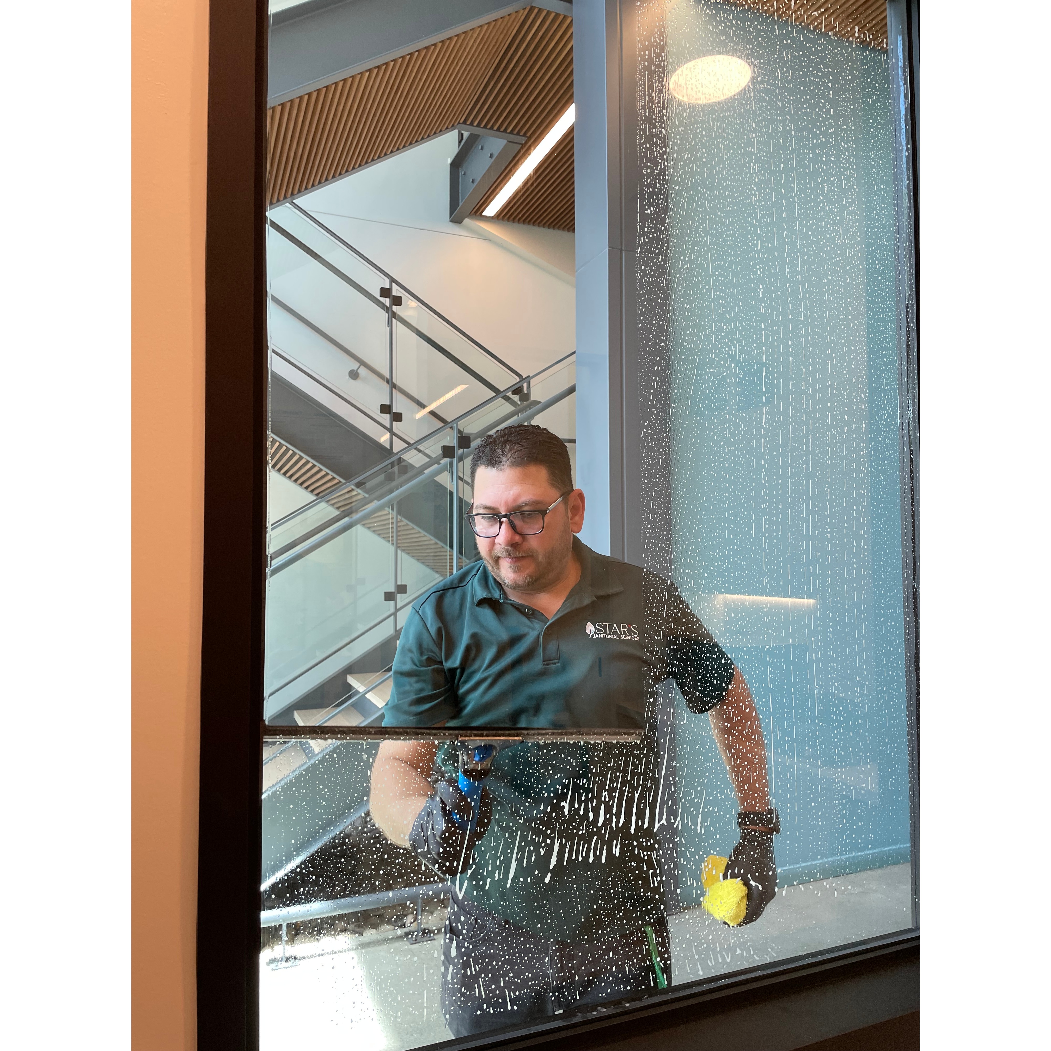 A Star's Janitorial Services team member cleaning interior glass windows in a commercial building for a streak-free finish.
