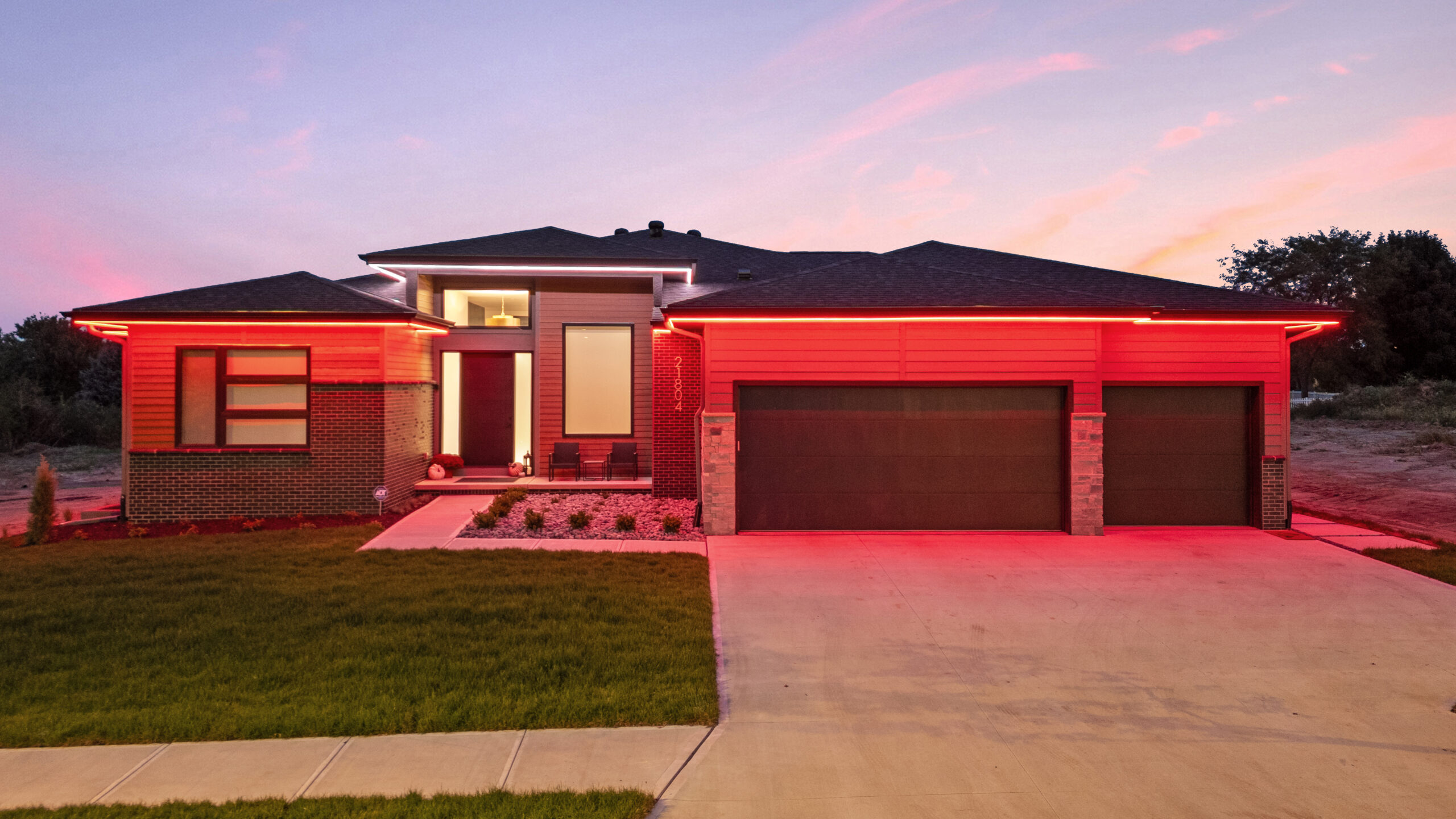 Red roofline and architectural lighting illuminating the front of a modern residential property.