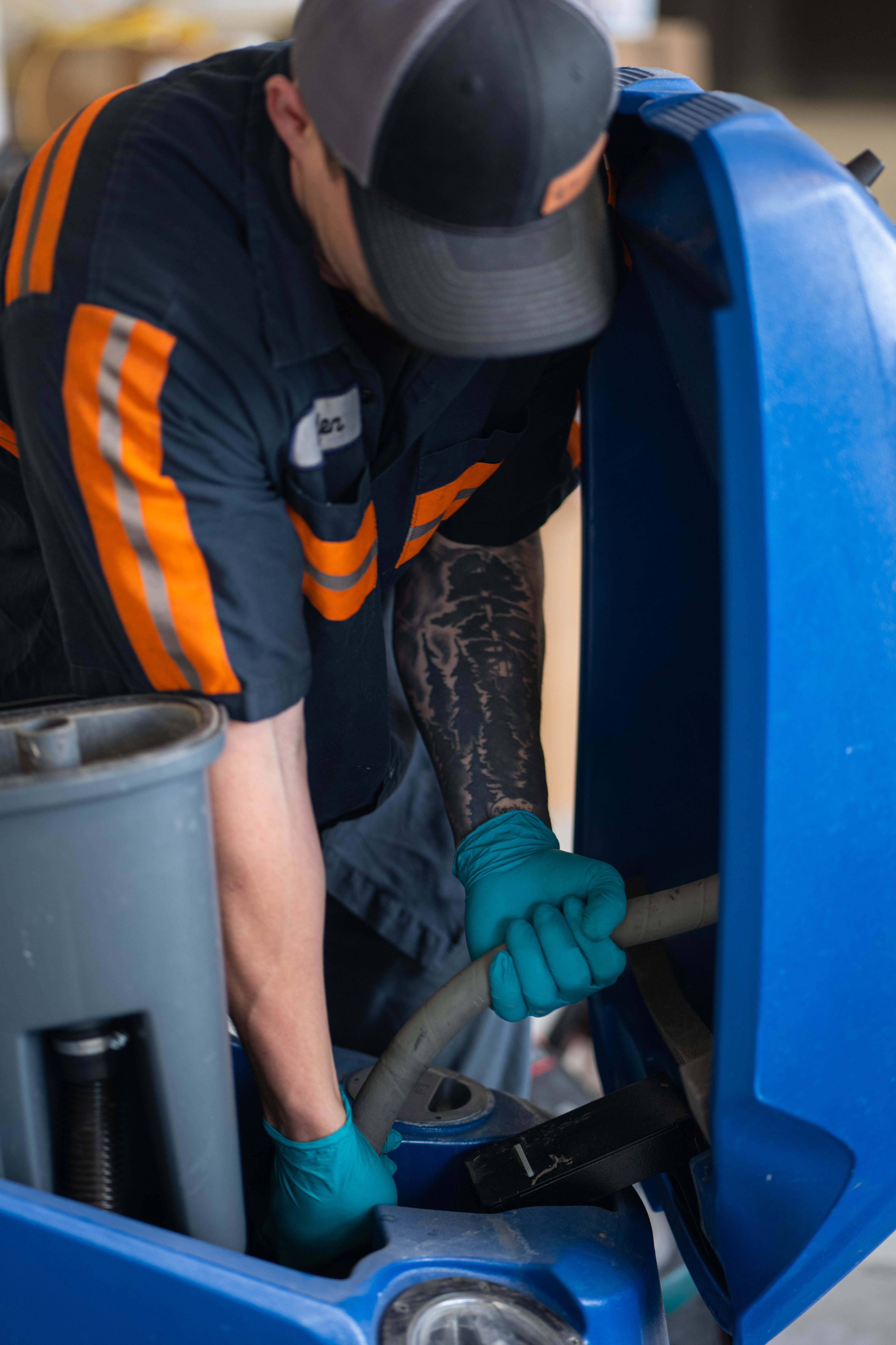 A certified WaySolutions technician performs a deep inspection of the vacuum hoses and recovery system inside a blue Kärcher Chariot stand-on floor scrubber. By expertly clearing blockages and optimizing suction power, our Layton-based team ensures your commercial cleaning equipment leaves behind perfectly dry and safe floors.