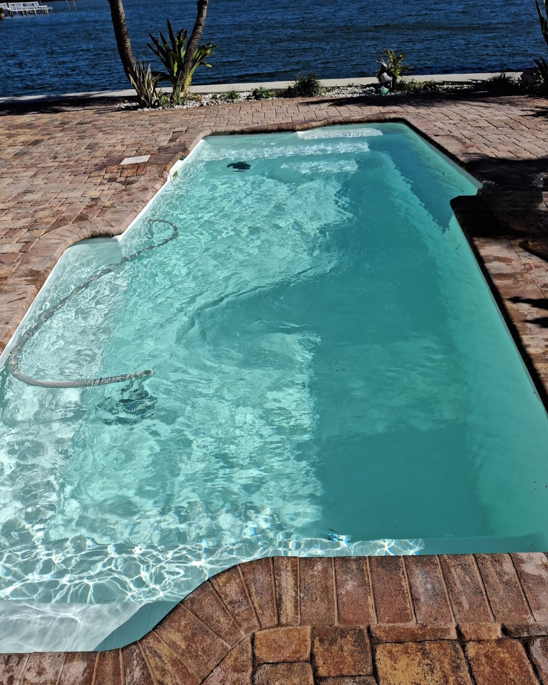 Long waterfront swimming pool with clear turquoise water, curved edges, stone decking, and open water views.