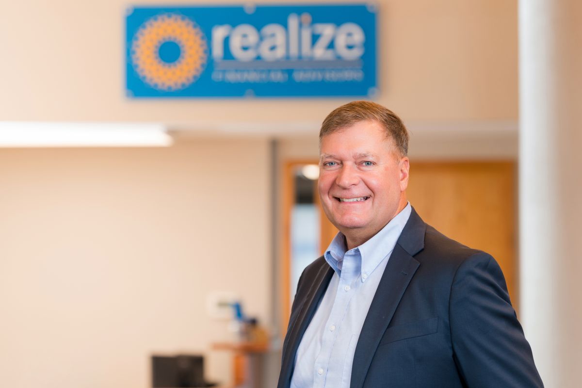 A headshot of a team member in a dark blazer standing in the entrance area of Realize Financial Advi 