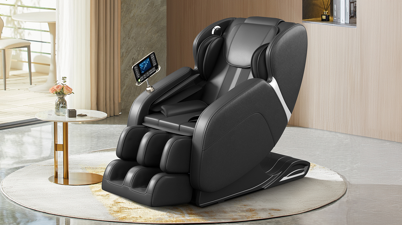 A black massage chair with a tablet mounted on the armrest is placed on a circular rug in a modern living room. A small marble-top side table with a vase of pink roses and a small black object sits next to the chair. In the background, large windows reveal an outdoor seating area, and a wooden wall features a decorative shelf with books and a diffuser.
